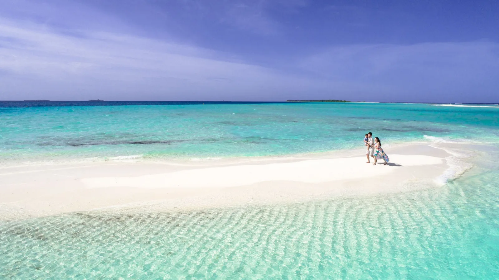 Aerial view of a couple walking on a picturesque sandbar in crystal-clear turquoise waters.